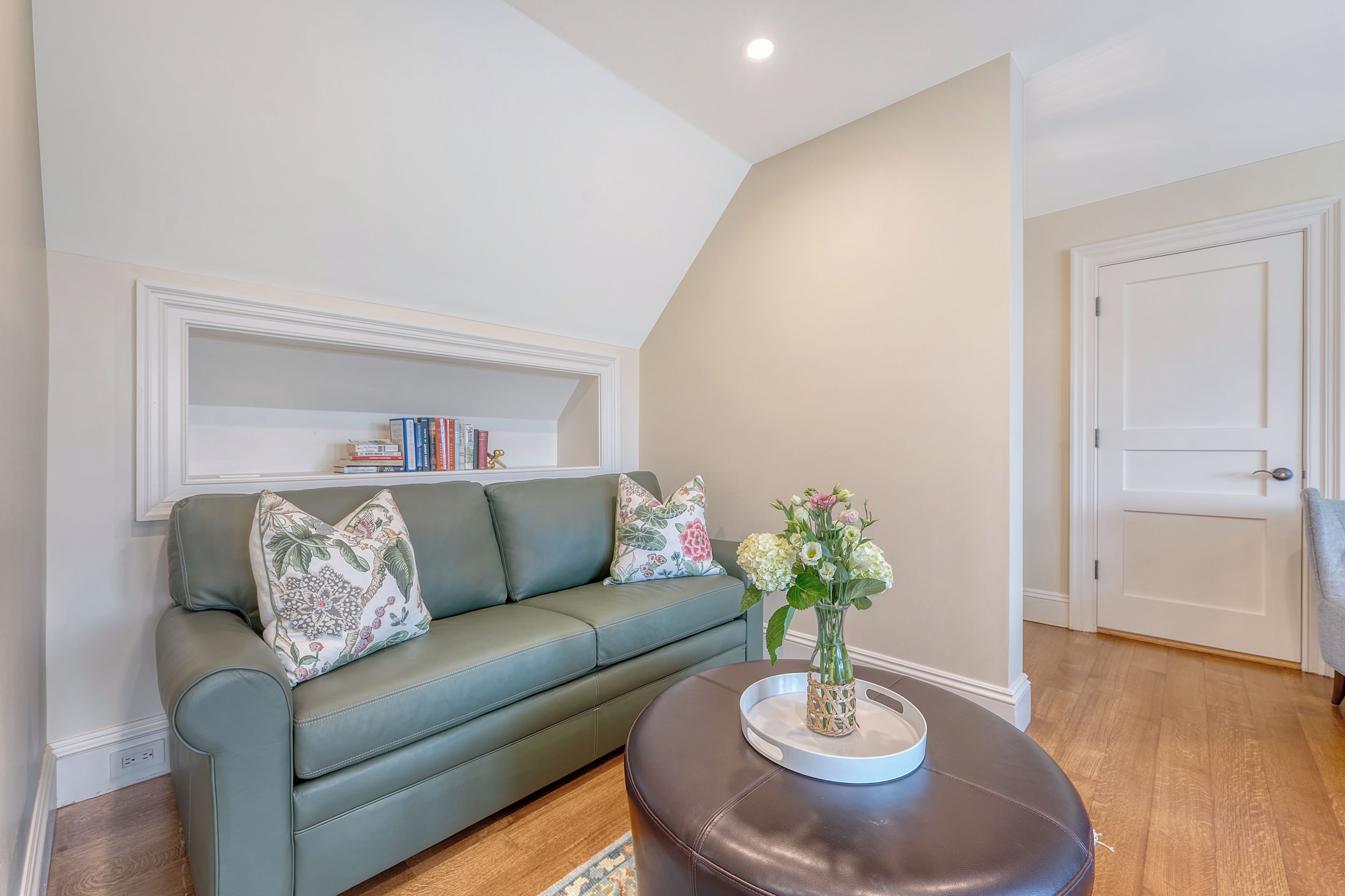 A living room with a green sofa, a coffee table with a vase, and a bookshelf.