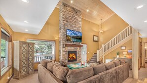 A cozy living room with a stone fireplace, a large sectional sofa, and a flat-screen TV mounted on the wall.