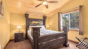 A bedroom with a wooden bed, a nightstand, a ceiling fan, and a window with curtains.
