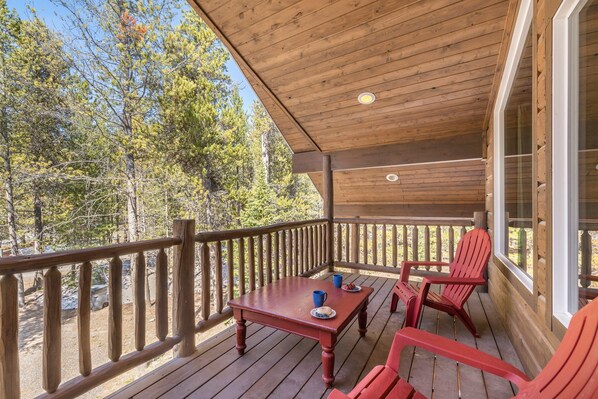 A wooden deck with a table and chairs, overlooking a forested area.