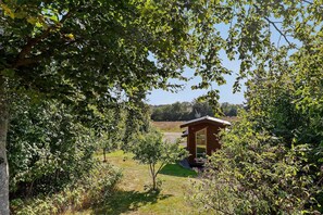 Eine Holzhütte mit einem großen Fenster, umgeben von dichtem Grün und blauem Himmel.