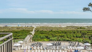 Vista a la playa desde un balcón con mobiliario exterior y sombrillas.