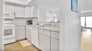 Una cocina moderna con armarios blancos, microondas, horno y cafetera.
