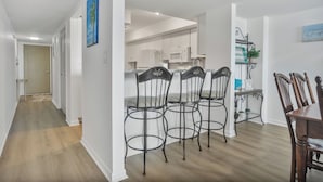 Una cocina moderna con armarios blancos, un comedor con mesa y sillas de madera, y un pasillo con una puerta y un cuadro.