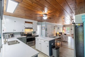 Une cuisine avec un plafond en bois, des armoires blanches, des appareils électroménagers en acier inoxydable et un coin repas comprenant une table et des chaises.