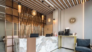 Un área de recepción moderna con mostrador de mármol, listones de madera e iluminación colgante.