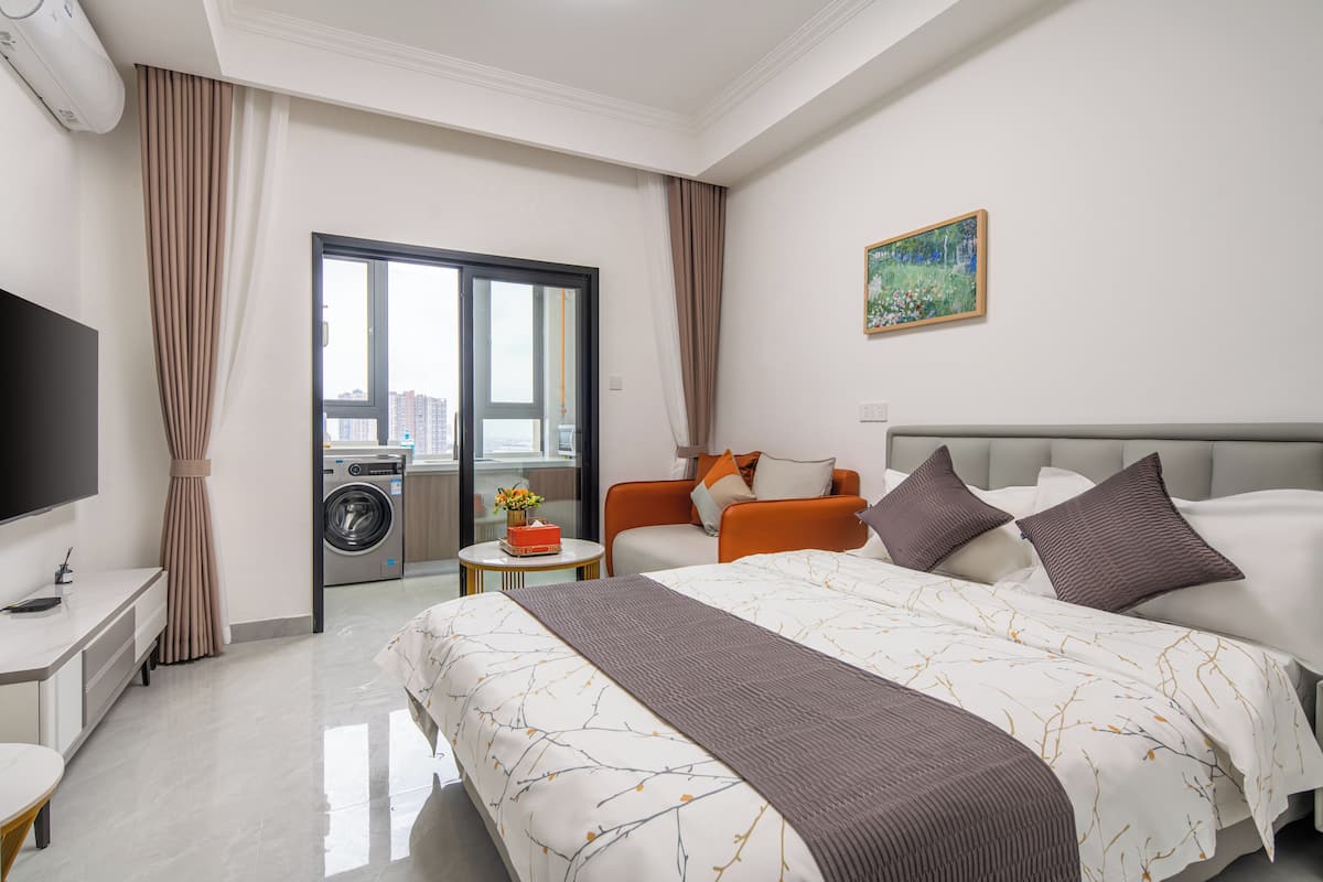Quarto de hotel com uma cama grande, televisão, máquina de lavar roupa e varanda com vista para a cidade.