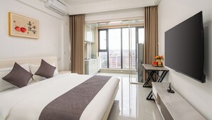 A hotel room with a large bed, a flat-screen TV, a small table with a vase of flowers, and a view of the city through the window. - Serveyou Apartment (Chengdu)