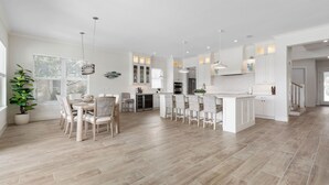 Una cocina amplia con armarios blancos, una isla central y un comedor con sillas.