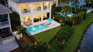 Una casa de dos pisos con piscina, patio cubierto y césped cuidado.