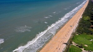 An aerial view of a coastal area with a sandy beach, a golf course, and a clear blue sky. - 3rd floor ocean views from Cinnamon Beach 235! (Palm Coast)