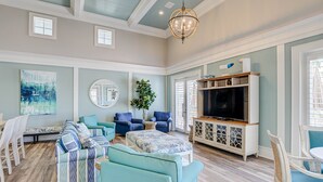 A spacious living room with teal sofas, a large TV, and a chandelier. - 3rd floor ocean views from Cinnamon Beach 235! (Palm Coast)
