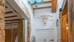Un pasillo con pared de piedra rústica, una puerta de madera, techo con vigas a la vista y un candelabro.