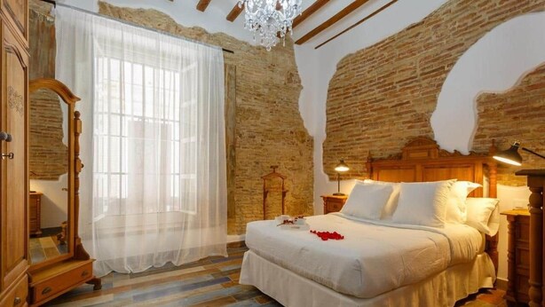 Un dormitorio con una cama grande, un armario de madera, un espejo, una araña y una pared de ladrillo.