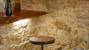 Un muro de piedra, una mesa redonda de madera, un sofá con cojines estampados y una botella de champán en un estante.