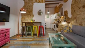 Un interior rústico con paredes de piedra vista, una zona de cocina y un área de estar con un sofá y una mesa de centro de vidrio.