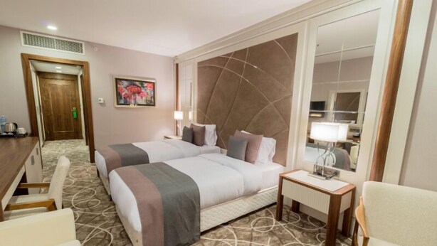 Une chambre d’hôtel avec deux lits, un coin salon comprenant une chaise, une petite table et un miroir.