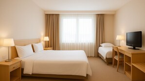 Une chambre d’hôtel avec un grand lit, un bureau avec une télévision, deux tables de chevet avec des lampes et une fenêtre avec des rideaux.