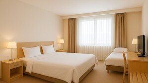 Une chambre d’hôtel avec un grand lit, deux tables de chevet avec des lampes, un bureau avec une télévision et une fenêtre avec des rideaux.