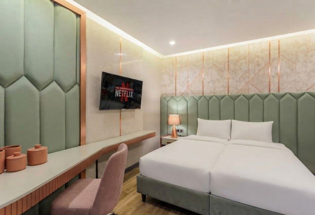 Une chambre d’hôtel équipée d’un lit, d’un bureau, d’une chaise, d’un téléviseur fixé au mur et d’une lampe de chevet.