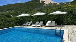 A swimming pool with lounge chairs and umbrellas, surrounded by greenery and a mountain backdrop. - Pet friendly apartment in Banjol with WiFi (Banjol)