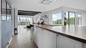A modern kitchen with a central island, white cabinetry, and a large sliding glass door leading to a patio. - Stunning home in Faaborg (Faaborg)