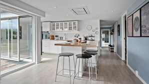 A modern kitchen with white cabinetry, a central island with stools, and a view through a glass door. - Stunning home in Faaborg (Faaborg)