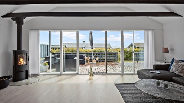 A modern living room with a large sliding glass door leading to an outdoor deck, a fireplace, and a cozy seating area. - Stunning home in Faaborg (Faaborg)