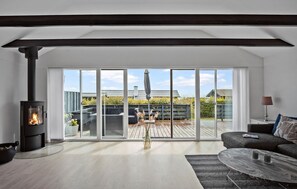 Una sala de estar moderna con un gran ventanal corredizo que da a una terraza exterior, una chimenea y una zona de estar acogedora.
