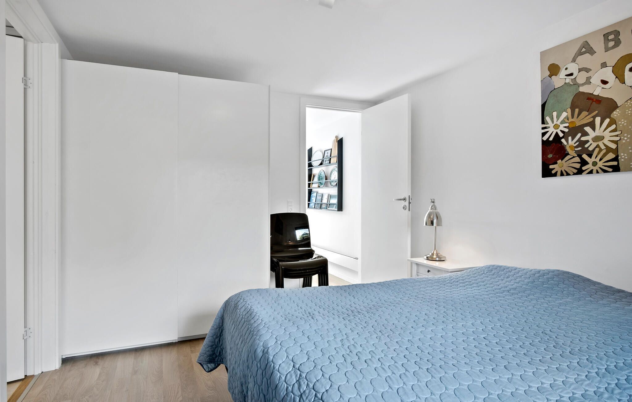 A bedroom with a bed, a chair, a desk, and a wall with a picture.