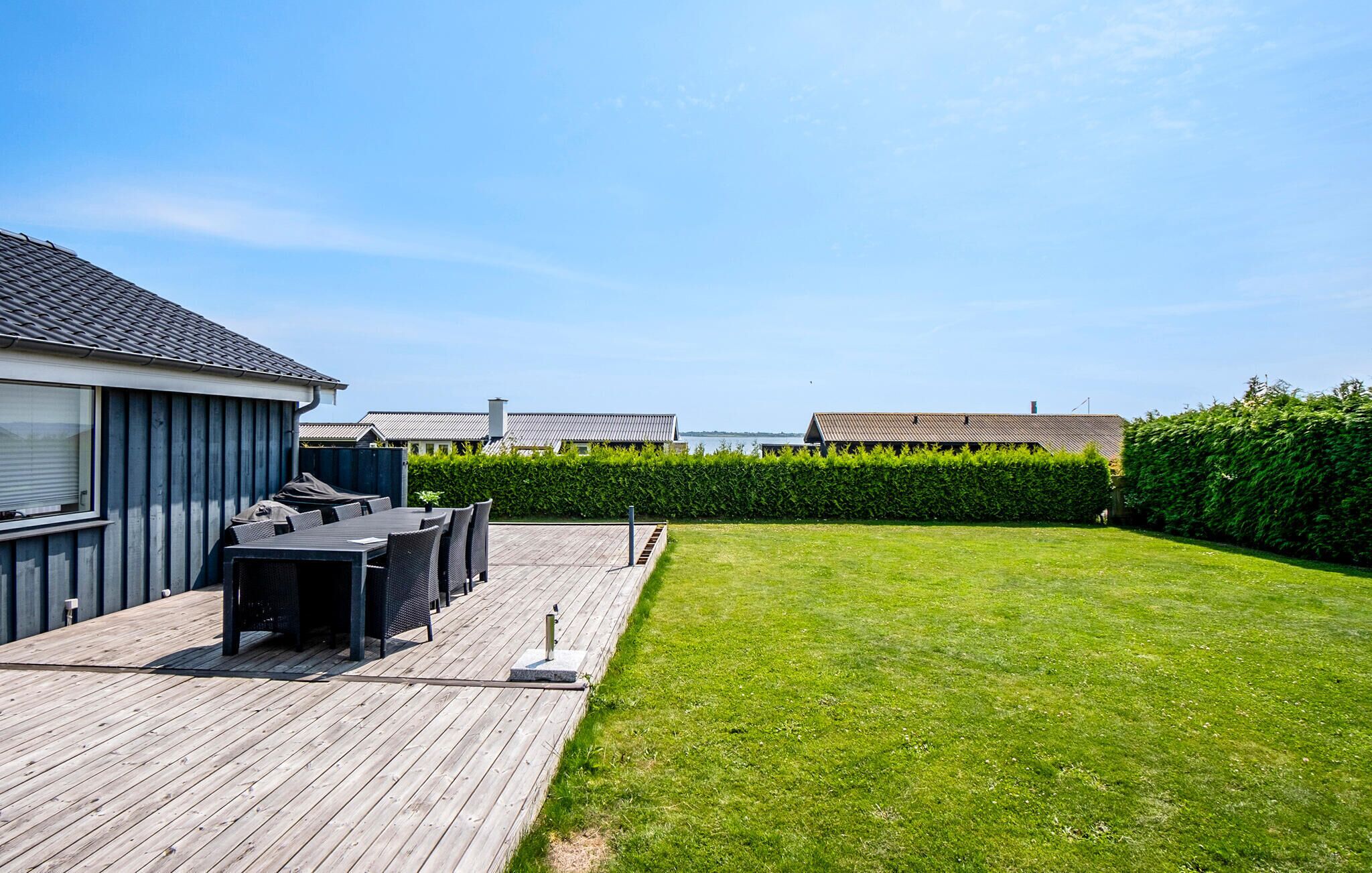 Ein Garten mit einer Holzterrasse, Gartenmöbeln und einem gepflegten Rasen.