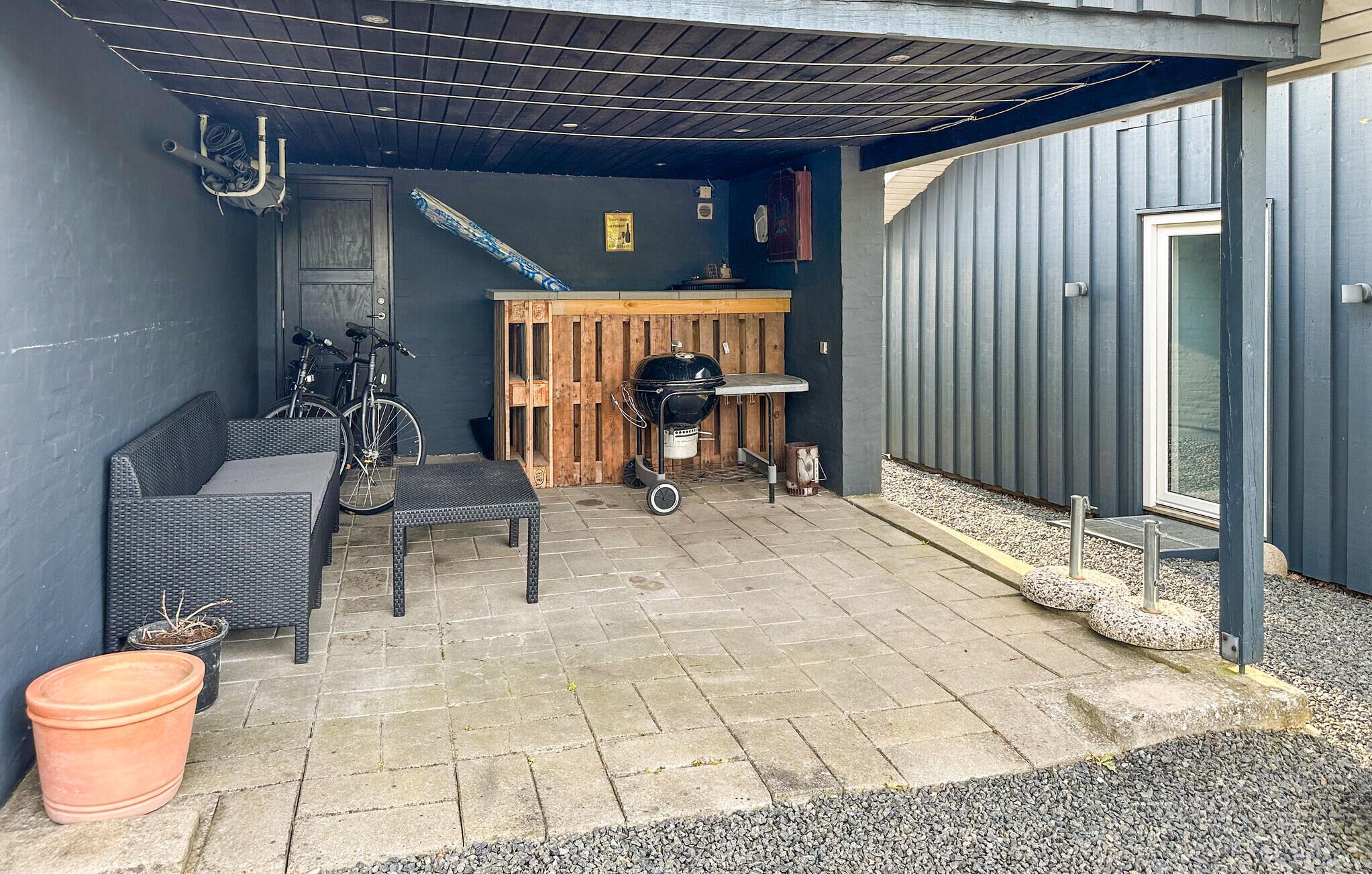 Un espace extérieur aménagé en terrasse, avec un barbecue, des meubles en osier et un vélo.