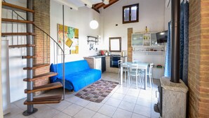 Ein kompakter Wohnraum mit einer Küche, Essbereich und einem blauen Sofa. Eine Treppe führt zu einer oberen Ebene.