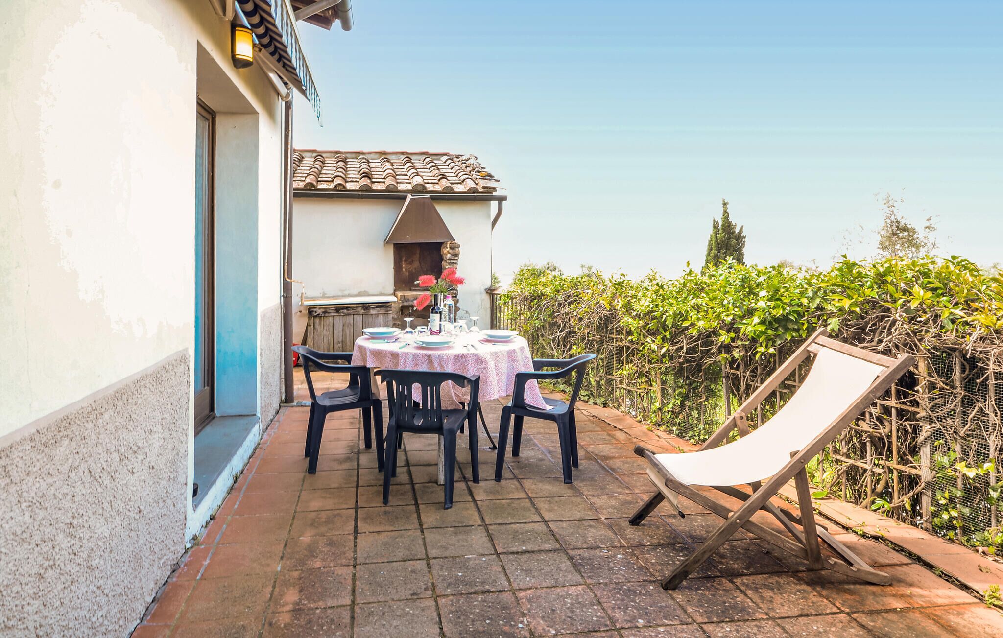 Eine Terrasse im Freien mit einem runden Tisch, Stühlen, einem Grill und einem Sessel mit weißem Kissen.
