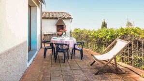 Eine Terrasse im Freien mit einem runden Tisch, Stühlen, einem Grill und einem Sessel mit weißem Kissen.