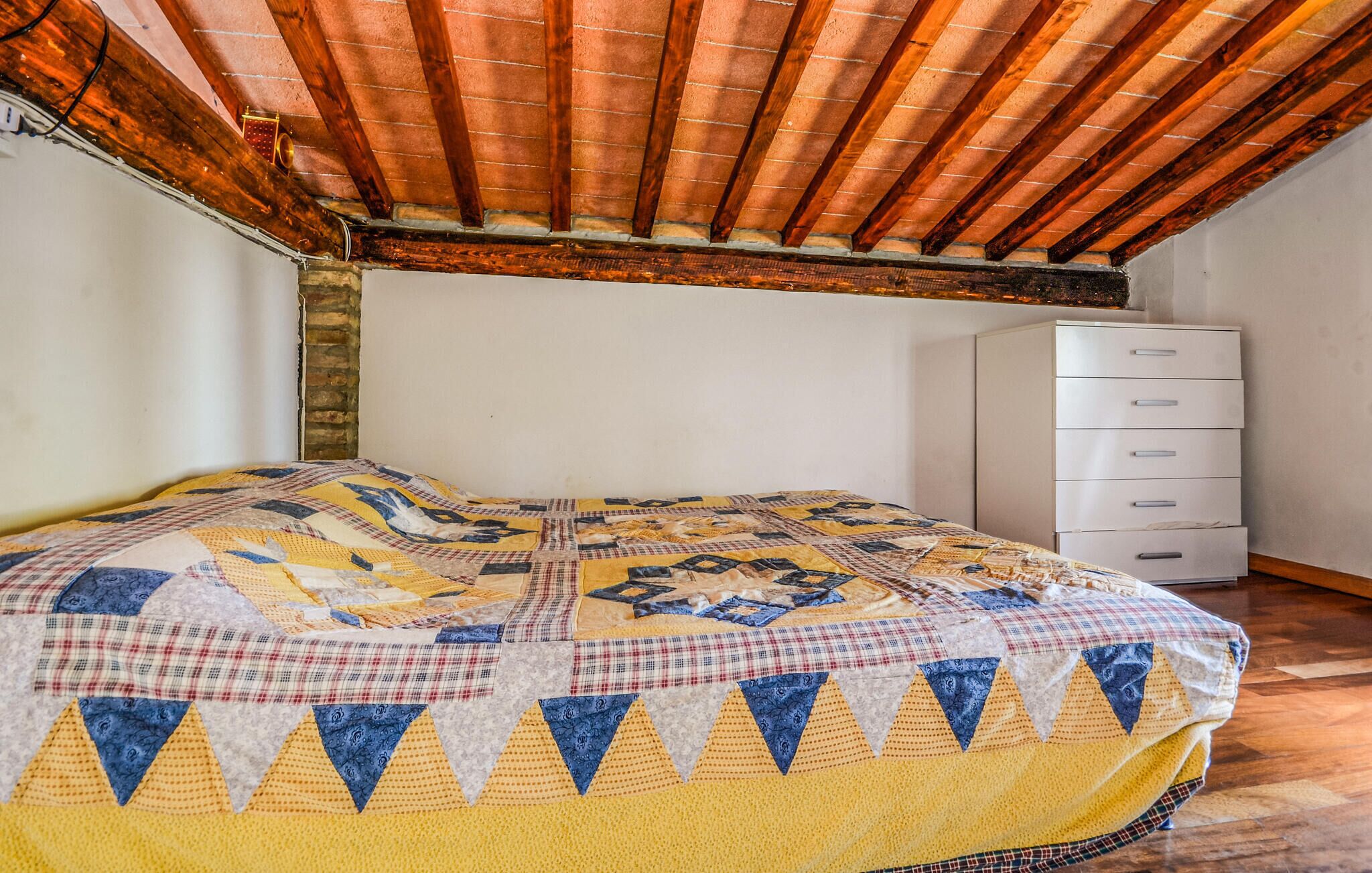 Ein Schlafzimmer mit Holzbalkendecke, einer gesteppten Bettdecke und einer weißen Kommode.
