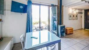 Ein Zimmer mit einem Glastisch, Stühlen, einem blauen Vorhang, einem Kamin und Blick ins Freie.