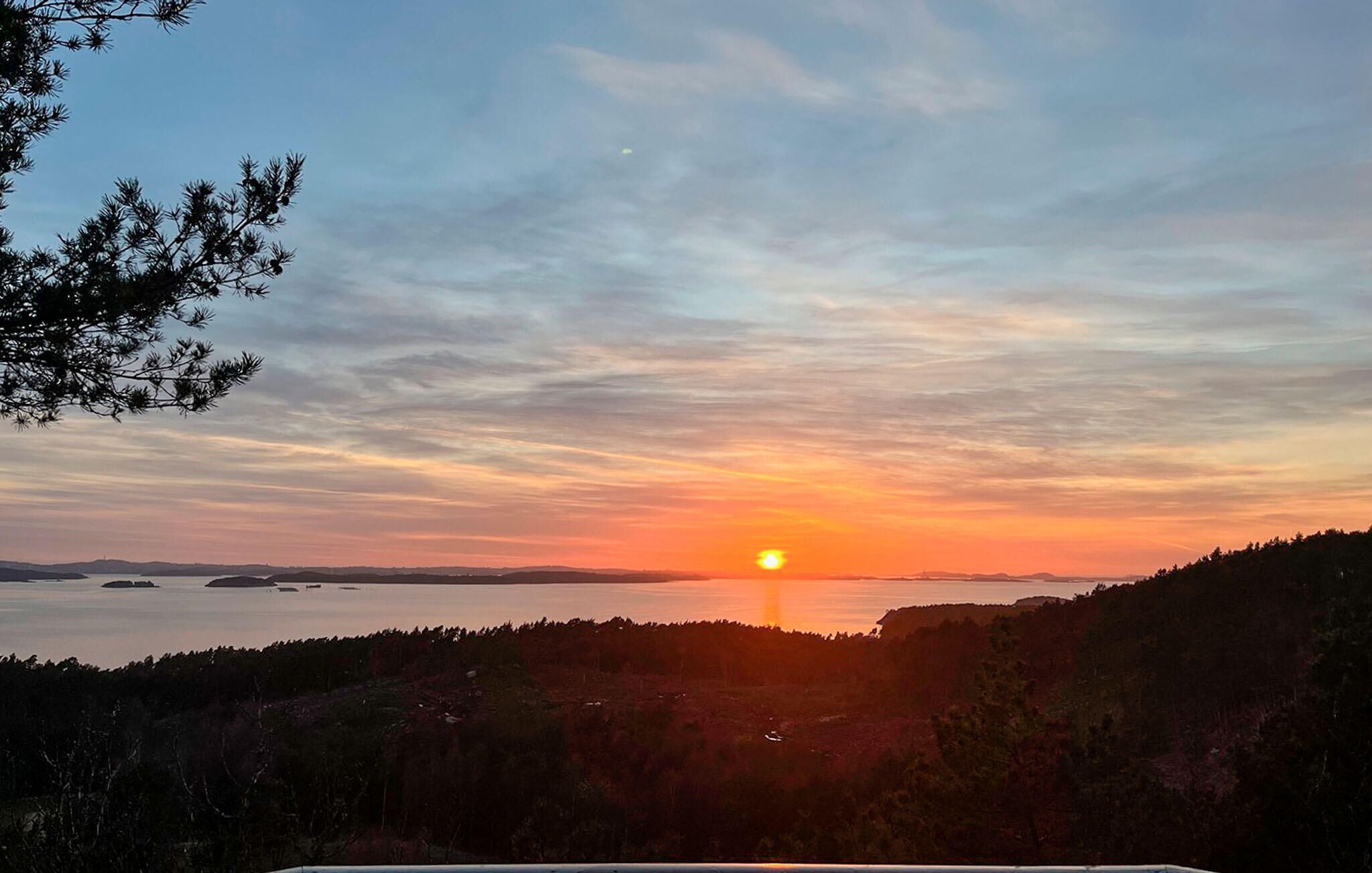 A sunset over a body of water with a forested hillside in the foreground.