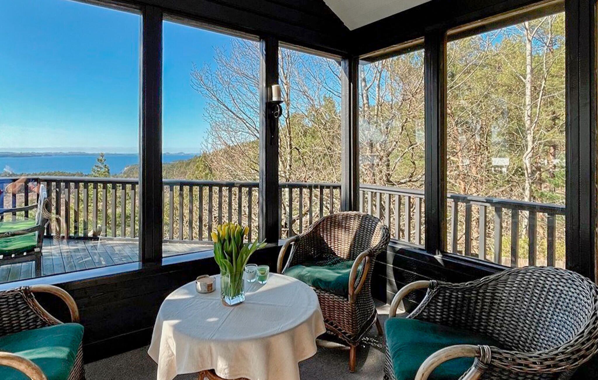 A sunlit room with large windows, wicker furniture, a round table, and a view of the sea.