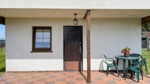 A house with a white exterior, a dark wooden door, a window, and a small patio area with a table and chairs.