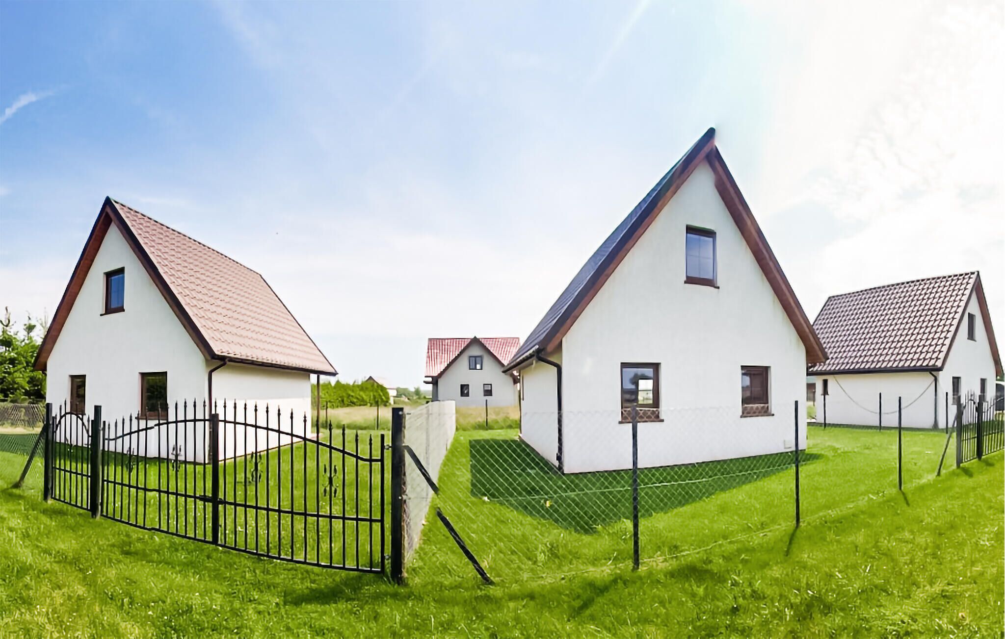 Une rangée de maisons blanches aux toits bruns, avec une clôture noire devant.