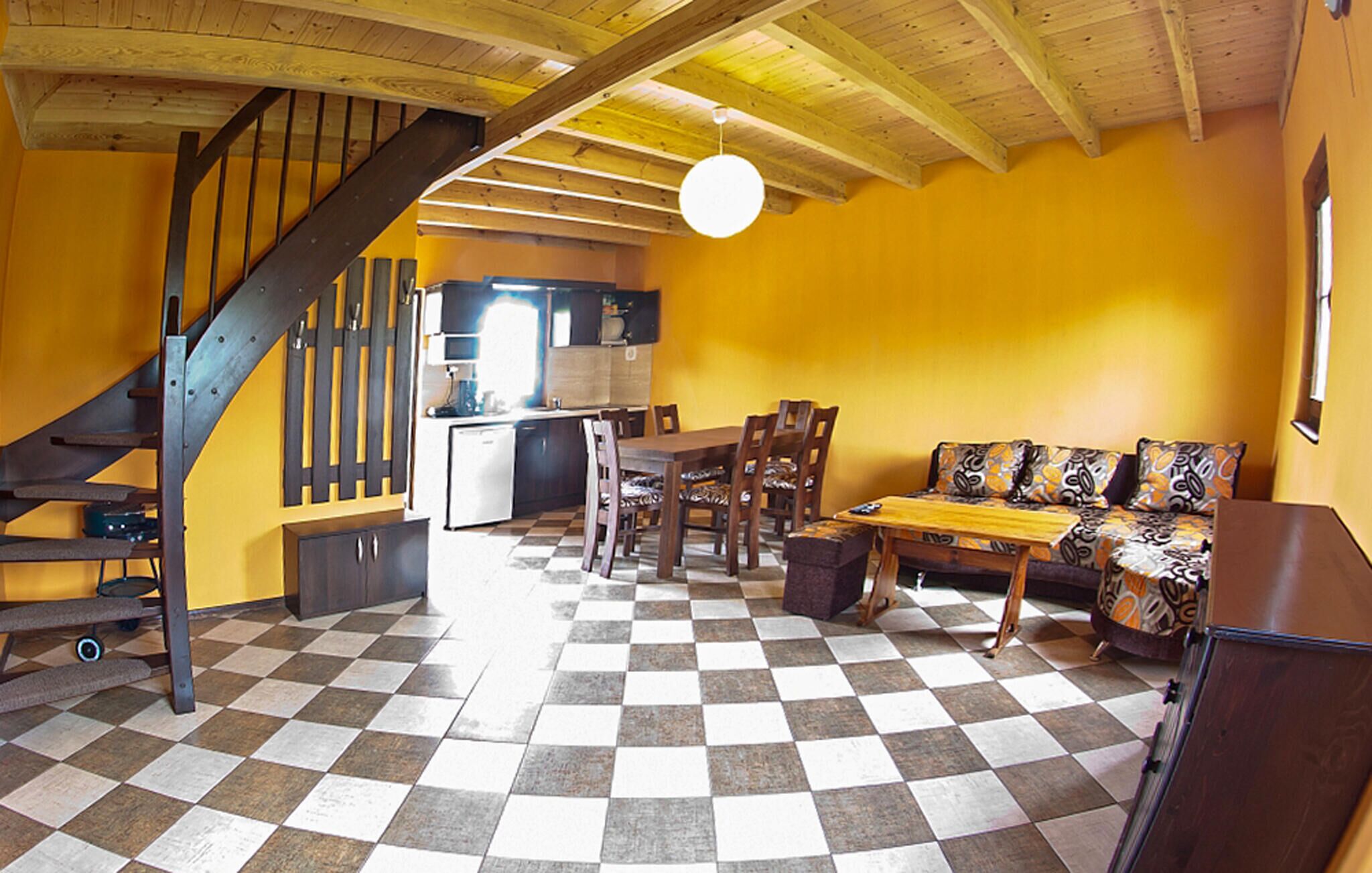 Una habitación con piso a cuadros, una escalera, un comedor con sillas y una mesa, y un sofá con cojines estampados.