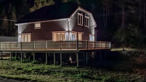 A two-story house with a balcony, wooden deck, and a dock extending into a body of water.
