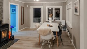 A dining area with a fireplace, white dining table, chairs, and a view of the outside through large windows.