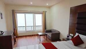 A hotel room with a bed, a desk, a chair, a small table, and a window with curtains. - HOTEL PHOENIX (Mussoorie)
