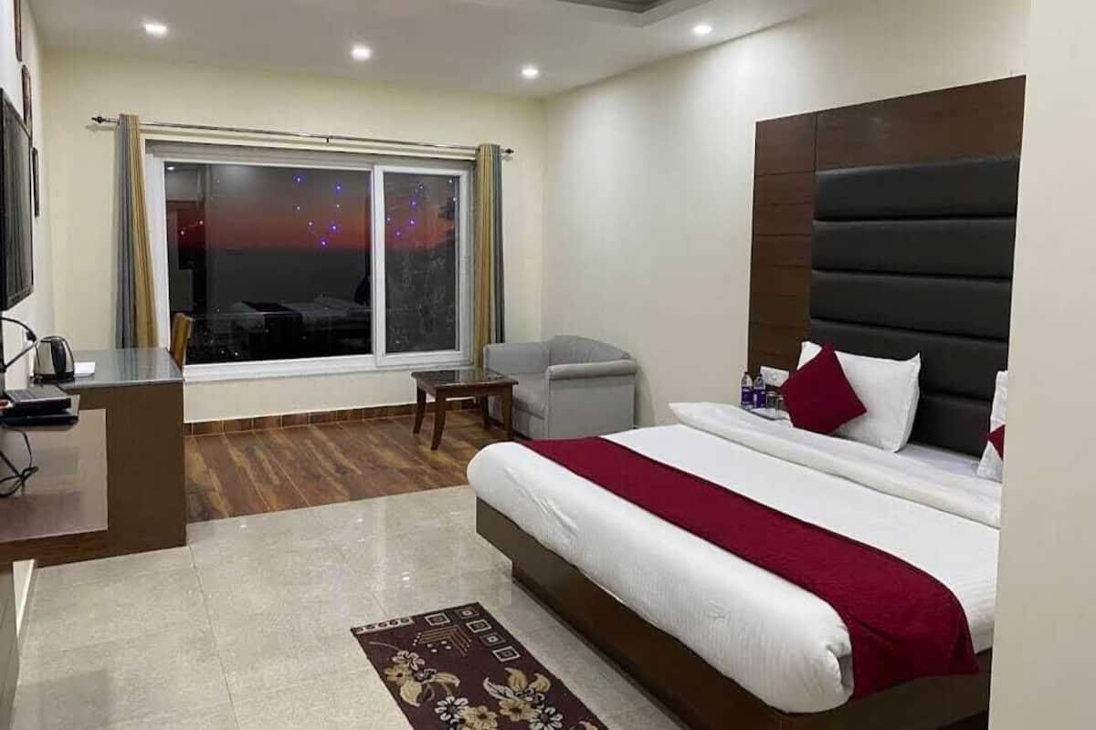 A hotel room with a large bed, a desk, a chair, and a window with a view of the cityscape.