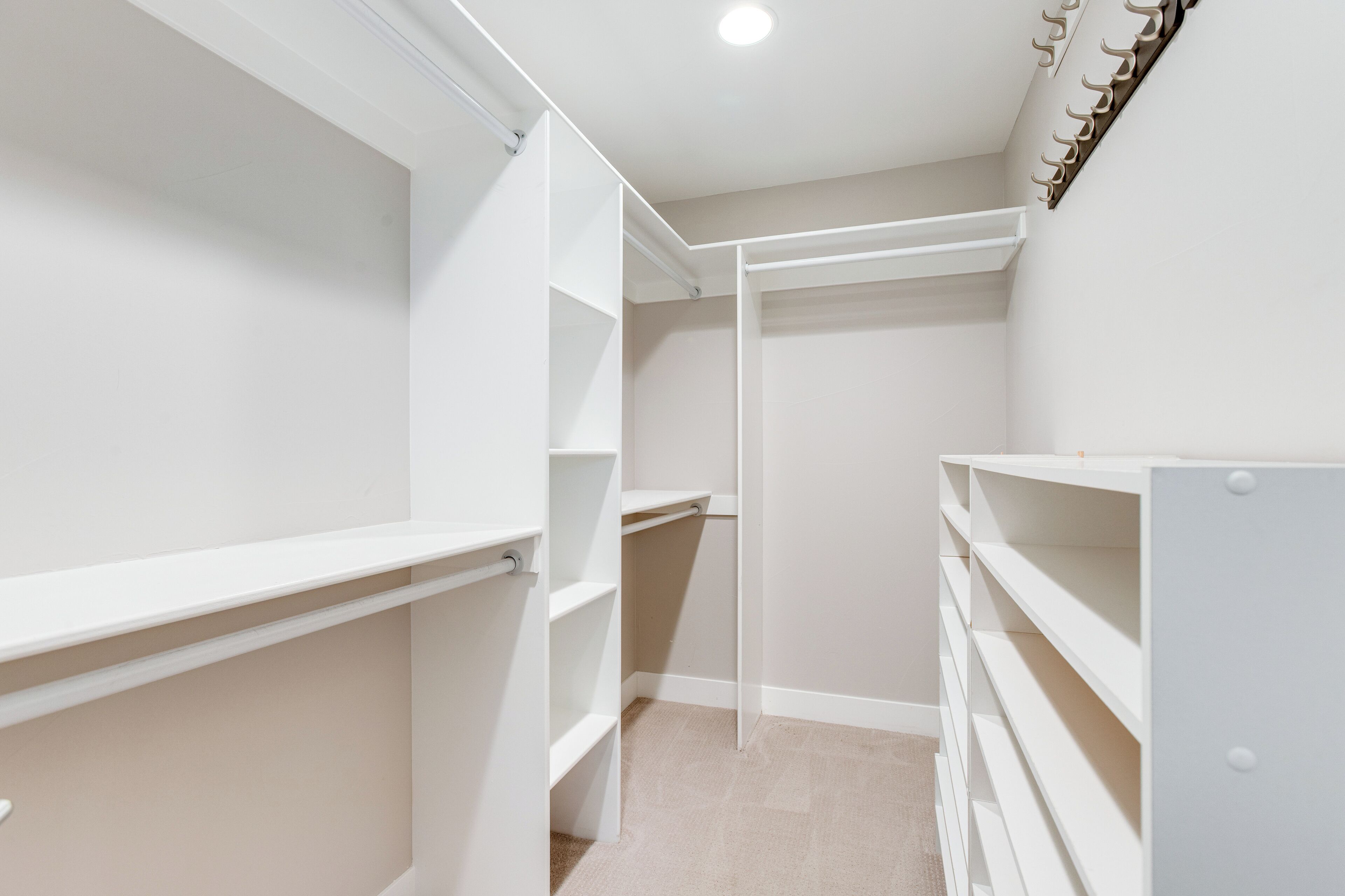 A walk-in closet with white shelving units and a hanging rod.