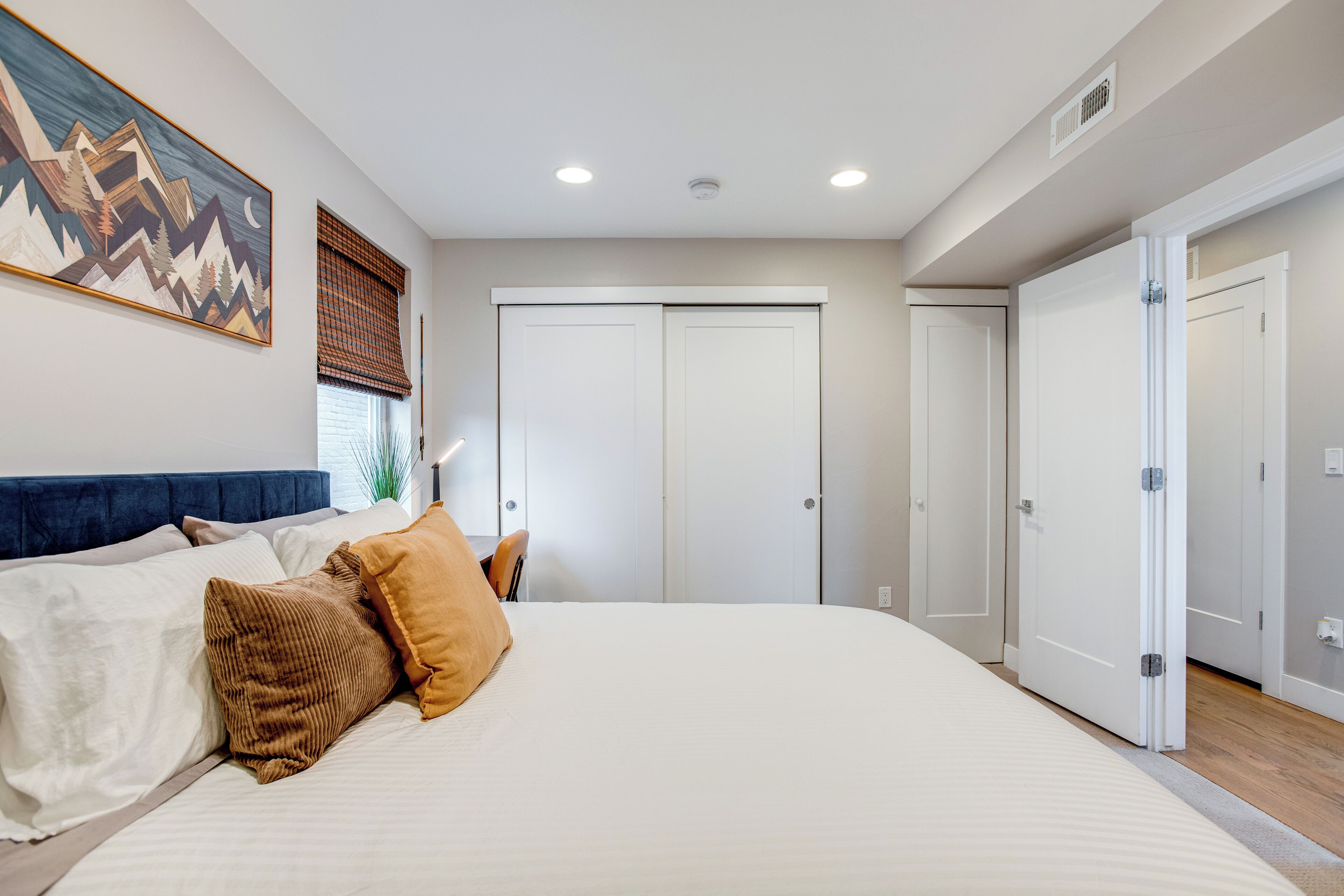 A bedroom with a large bed, a headboard, a painting, and a closet with sliding doors.