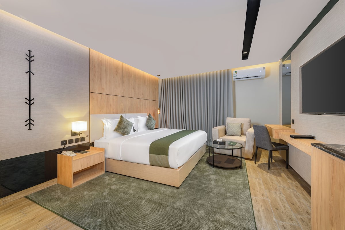 A modern hotel room with a large bed, bedside tables, a desk, a chair, and a TV.