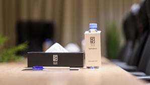A hotel room with a bedside table, a tissue box, a pen, and a water bottle. - Aryash hotel  (Abha)